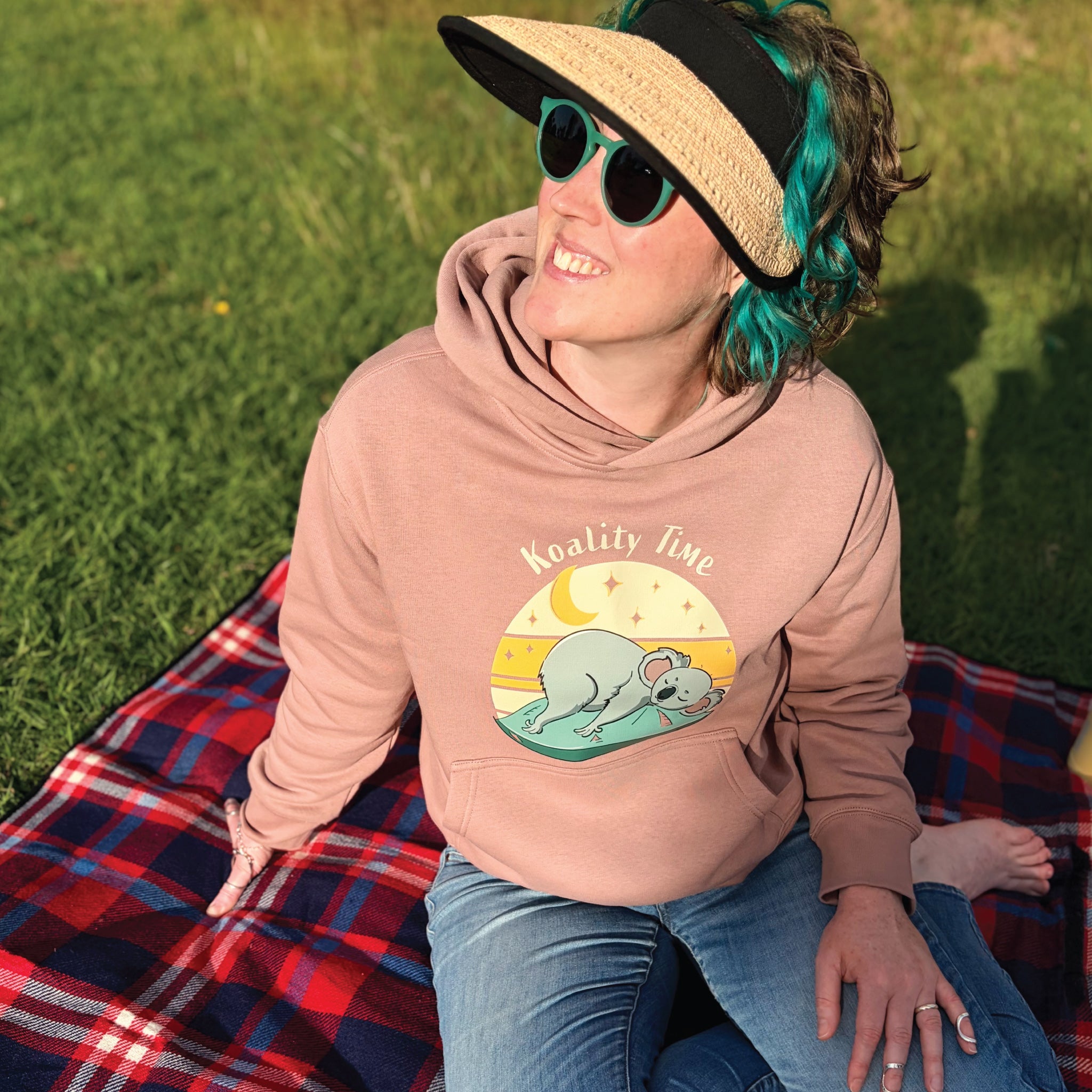 Woman wearing a hazy pink Women's Koala Hoodie featuring a hand-drawn koala illustration and "Koality Time" slogan, enjoying a relaxed outdoor lifestyle setting in a cosy and comfortable hoodie.