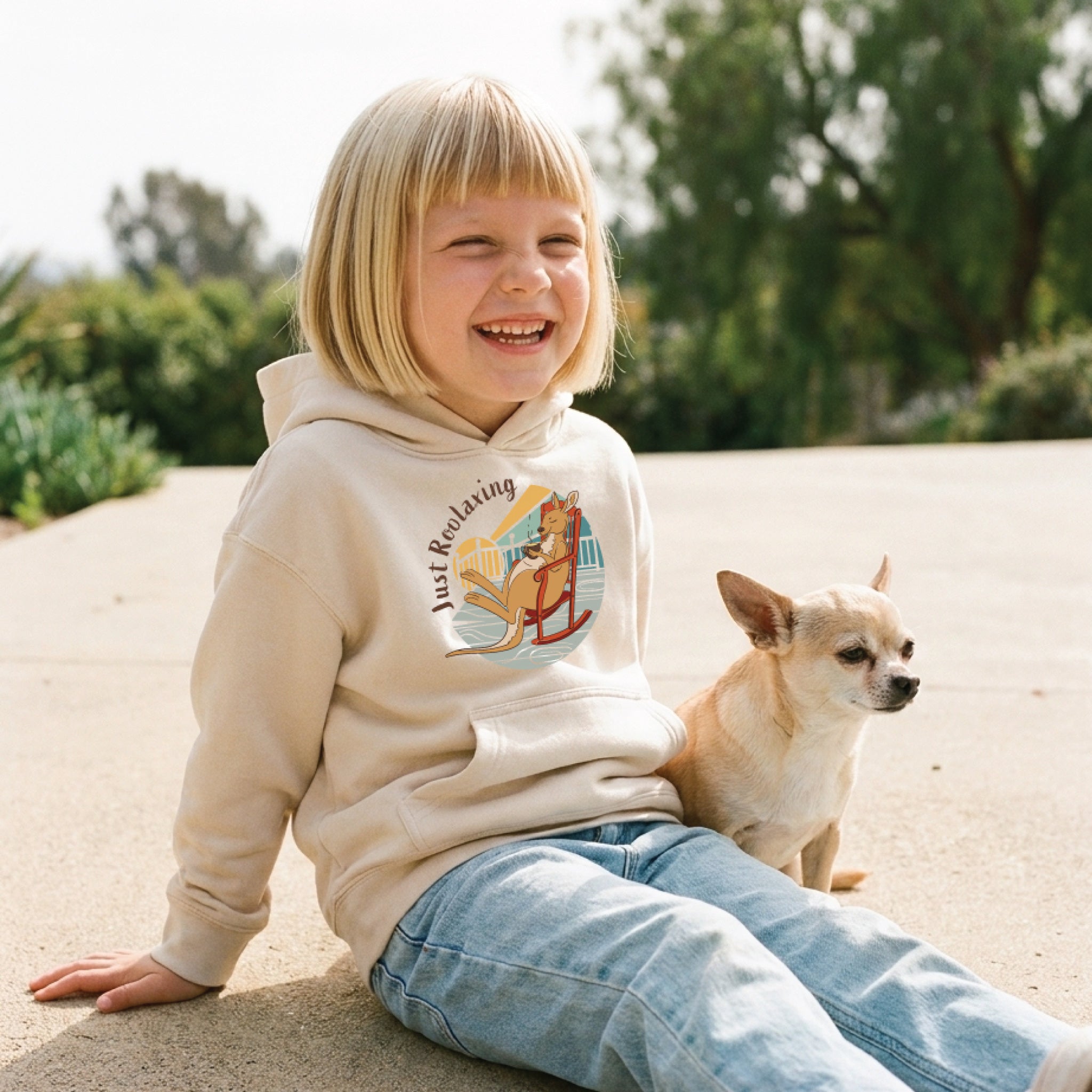 Child wearing a Kids' Kangaroo Hoodie featuring a hand-drawn kangaroo illustration and "Just Roolaxing" slogan, enjoying a fun and relaxed outdoor lifestyle setting.