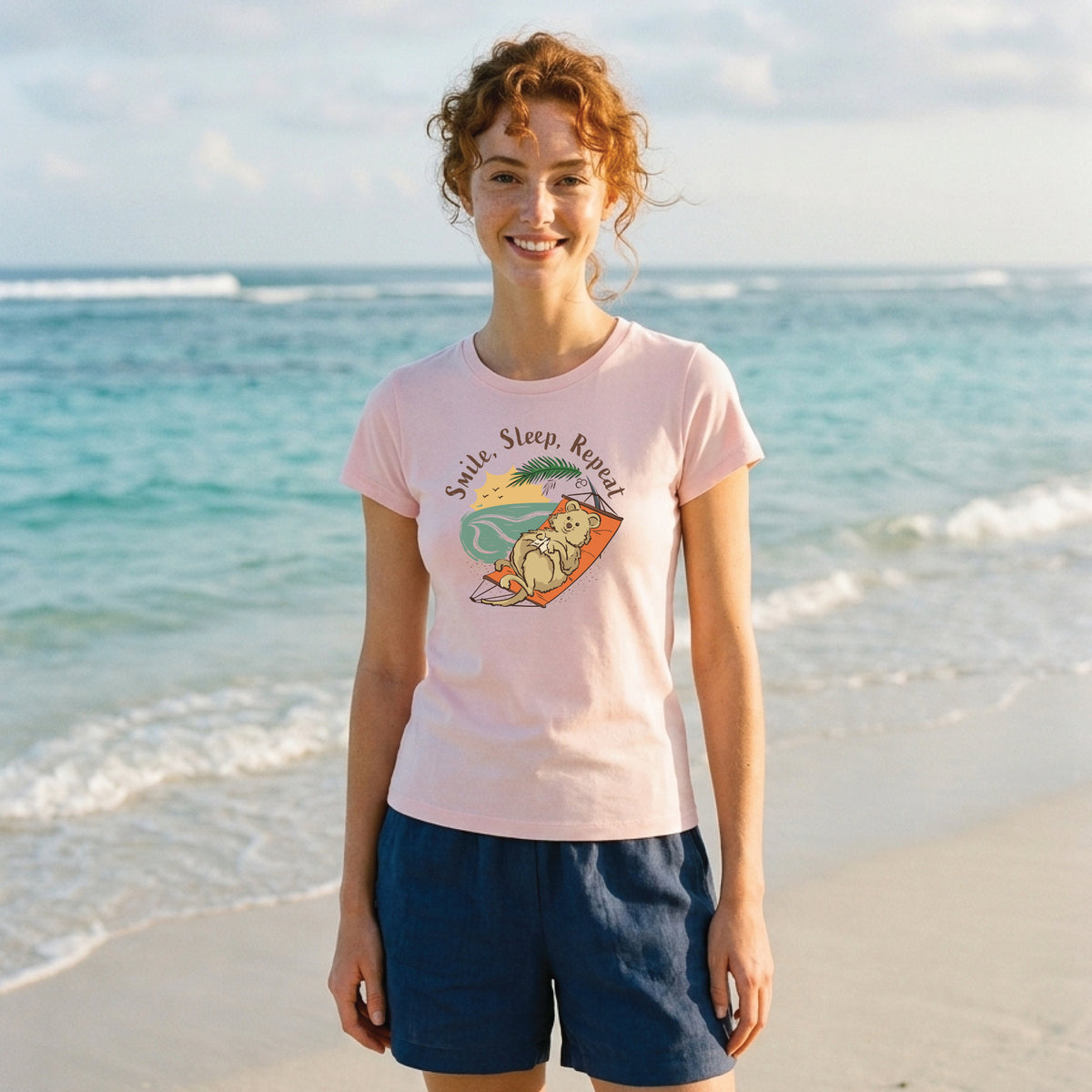 Woman wearing a Pink Women's Quokka T-Shirt featuring a hand-drawn quokka illustration and "Smile, Sleep, Repeat" slogan, enjoying a relaxed outdoor lifestyle setting.