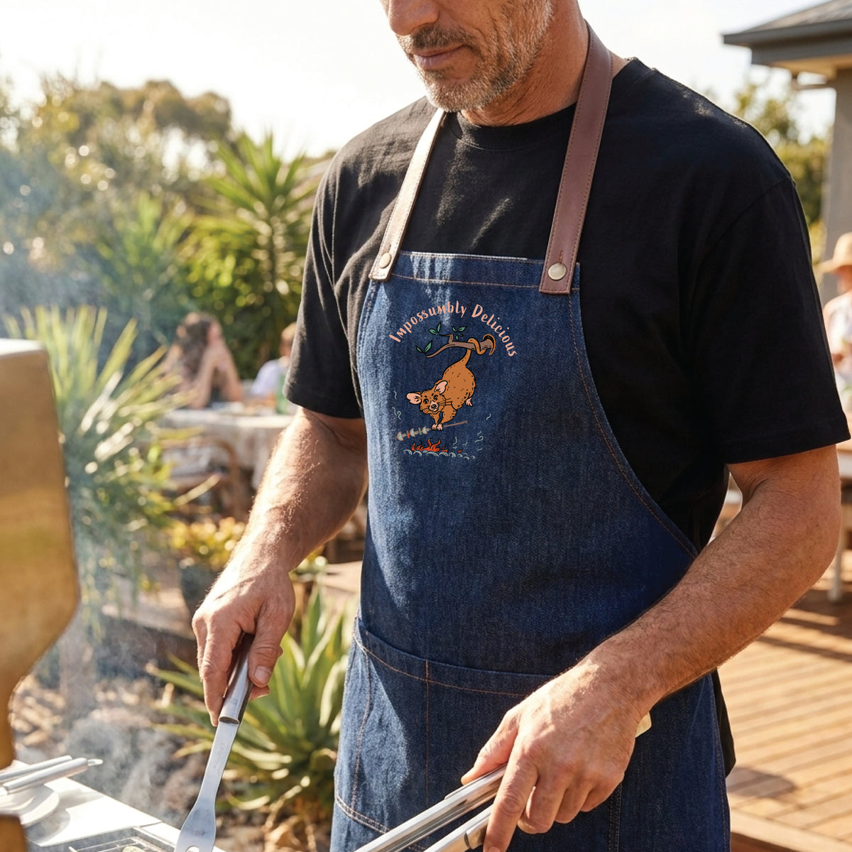 Possum BBQ denim apron featuring a hand-drawn possum cooking over an open fire with Impossumbly Delicious slogan
