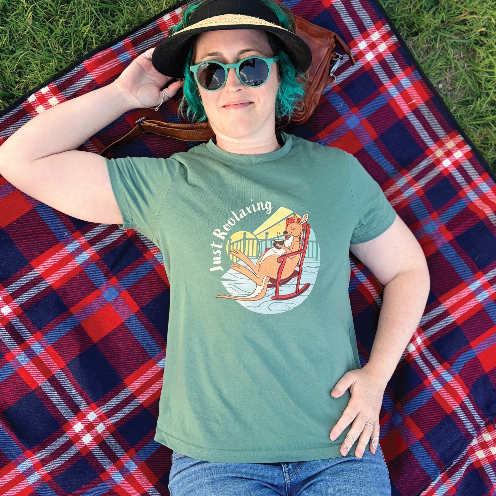 Woman wearing a Sage Women's Kangaroo T-Shirt featuring a hand-drawn kangaroo illustration and "Just Roolaxing" slogan, enjoying a relaxed outdoor lifestyle setting.