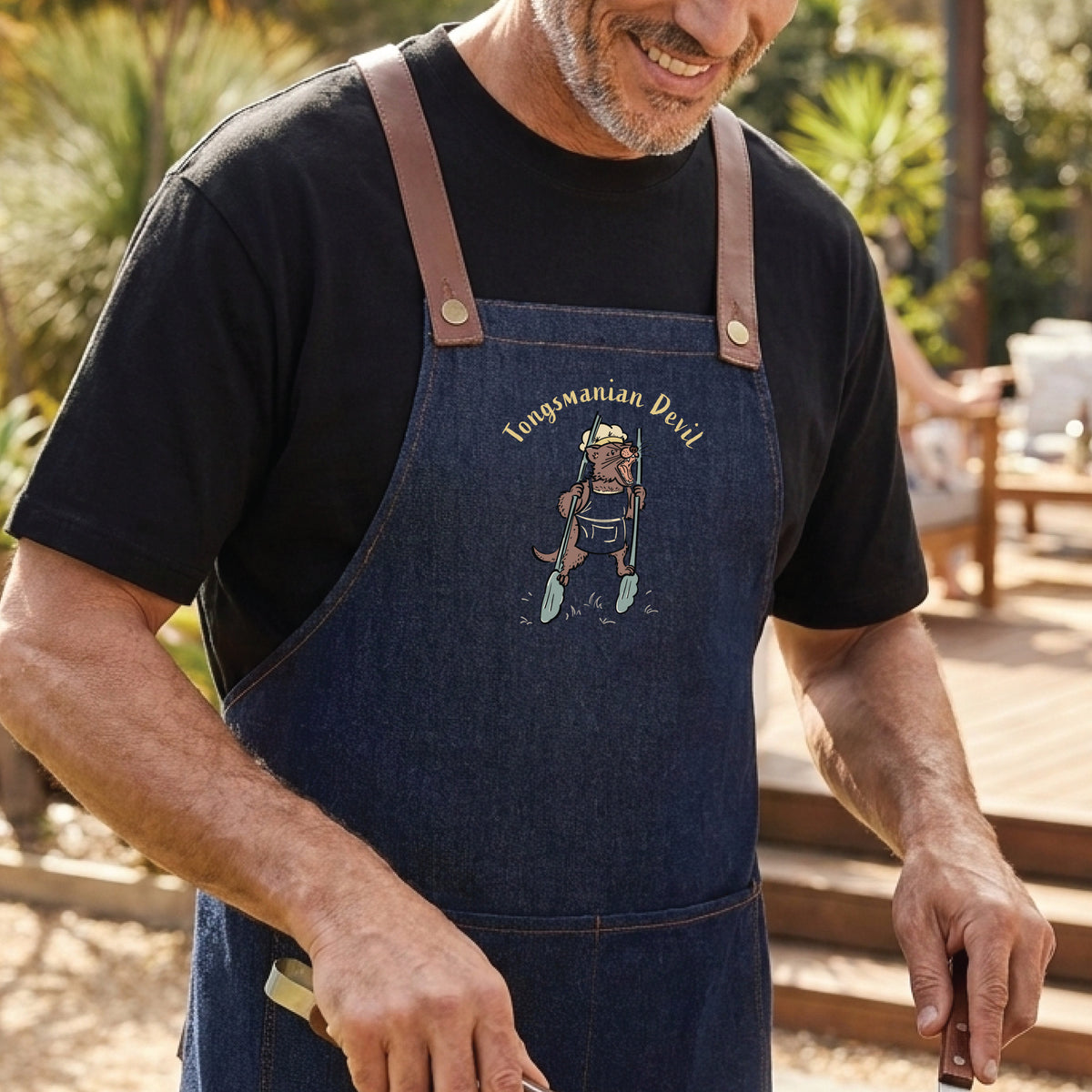 Tasmanian Devil BBQ denim apron featuring a hand-drawn Tassie devil holding cooking tongs with Tongsmanian Devil slogan