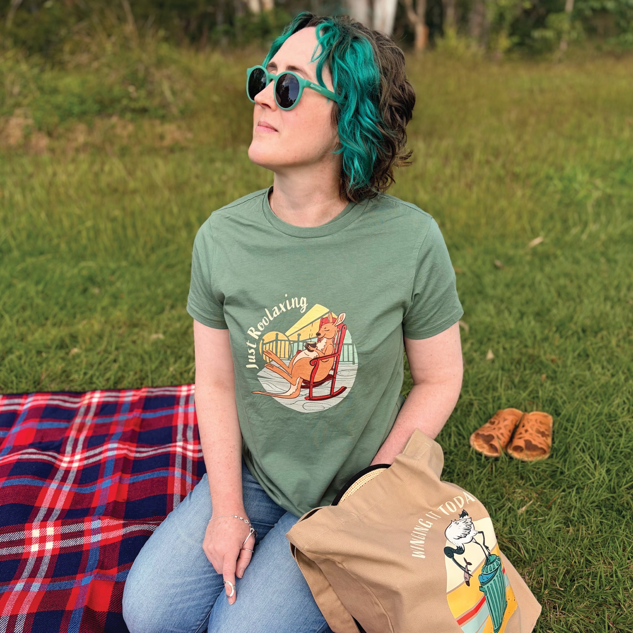 Woman wearing a Women's Kangaroo T-Shirt featuring a hand-drawn kangaroo illustration and "Just Roolaxing" slogan, enjoying a relaxed outdoor lifestyle setting.
