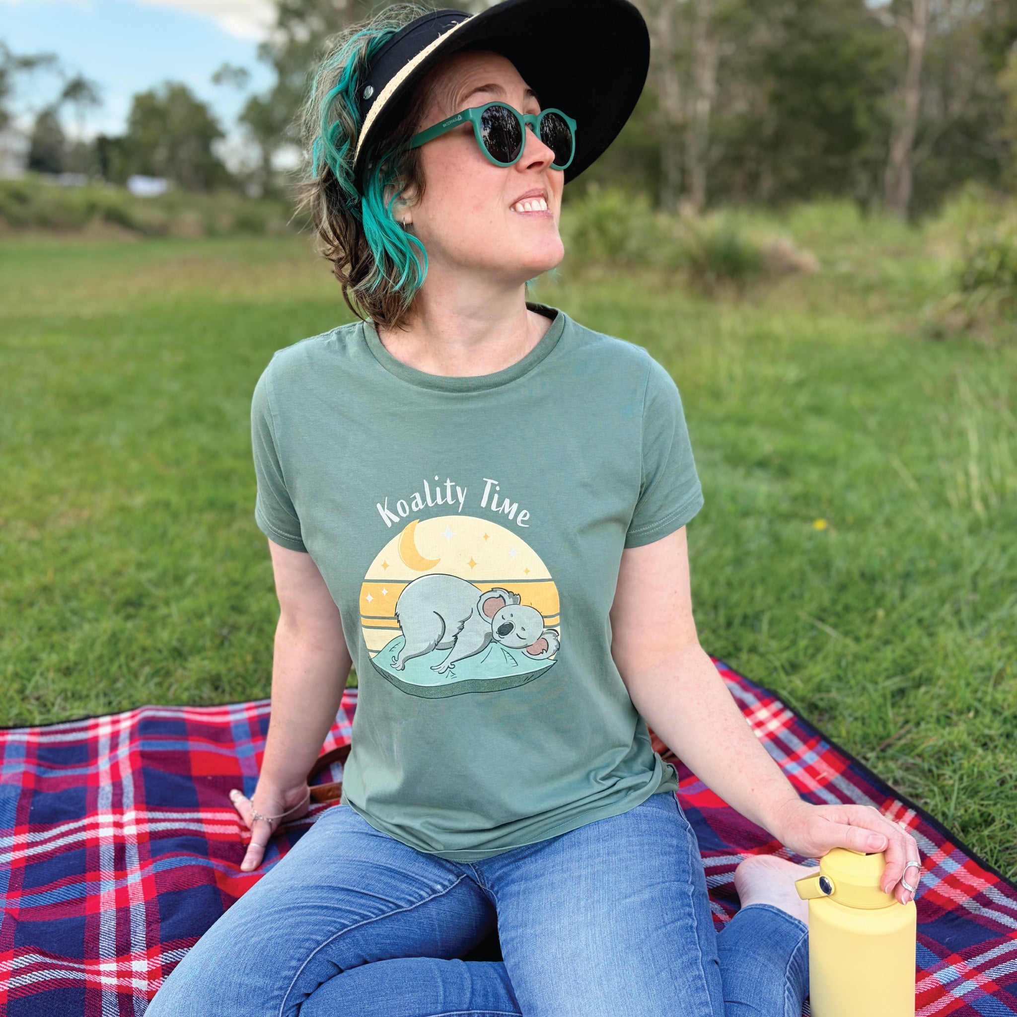 Woman wearing a Women's Koala T-Shirt featuring a hand-drawn koala illustration and "Koality Time" slogan, enjoying a relaxed outdoor lifestyle setting.